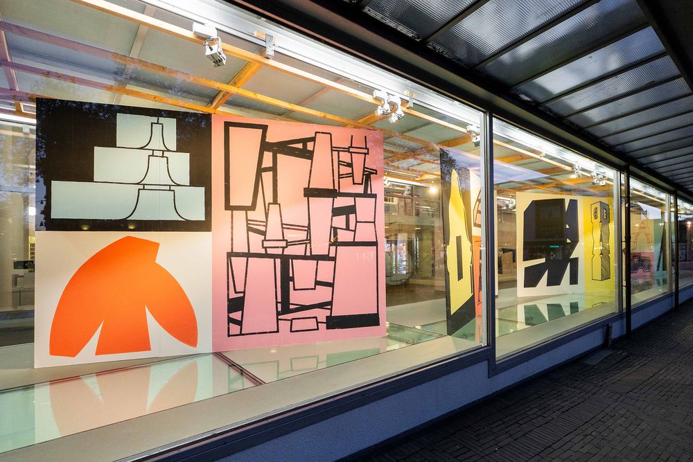 Verlichte vitrines van SCHUNCK met kleurrijke grafische kunstwerken van Jeroen Erosie, gezien vanaf de straat in de avond.