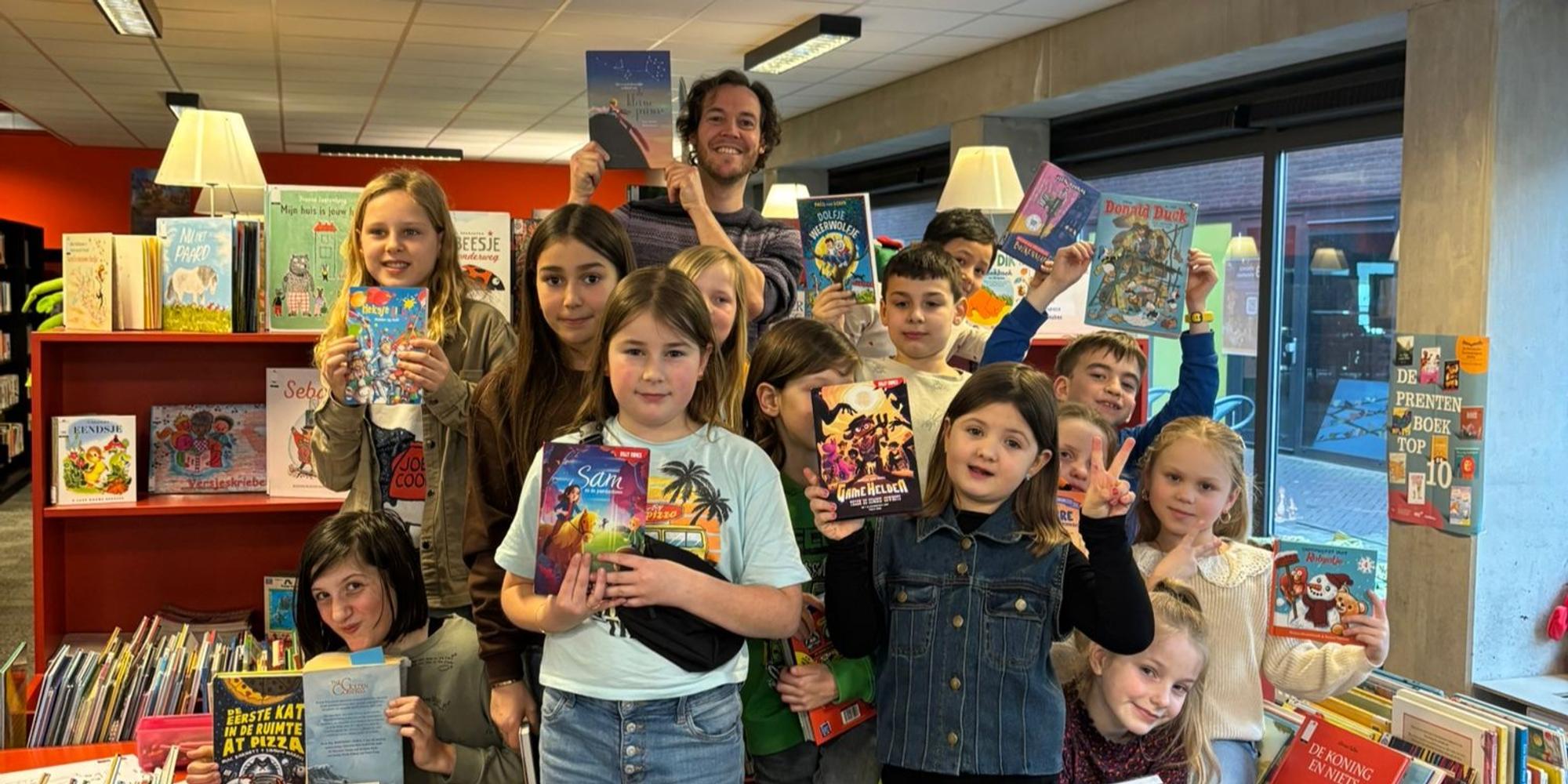 Groep kinderen in een boekwinkel houdt verschillende kleurrijke kinderboeken omhoog, omringd door volle boekenrekken.