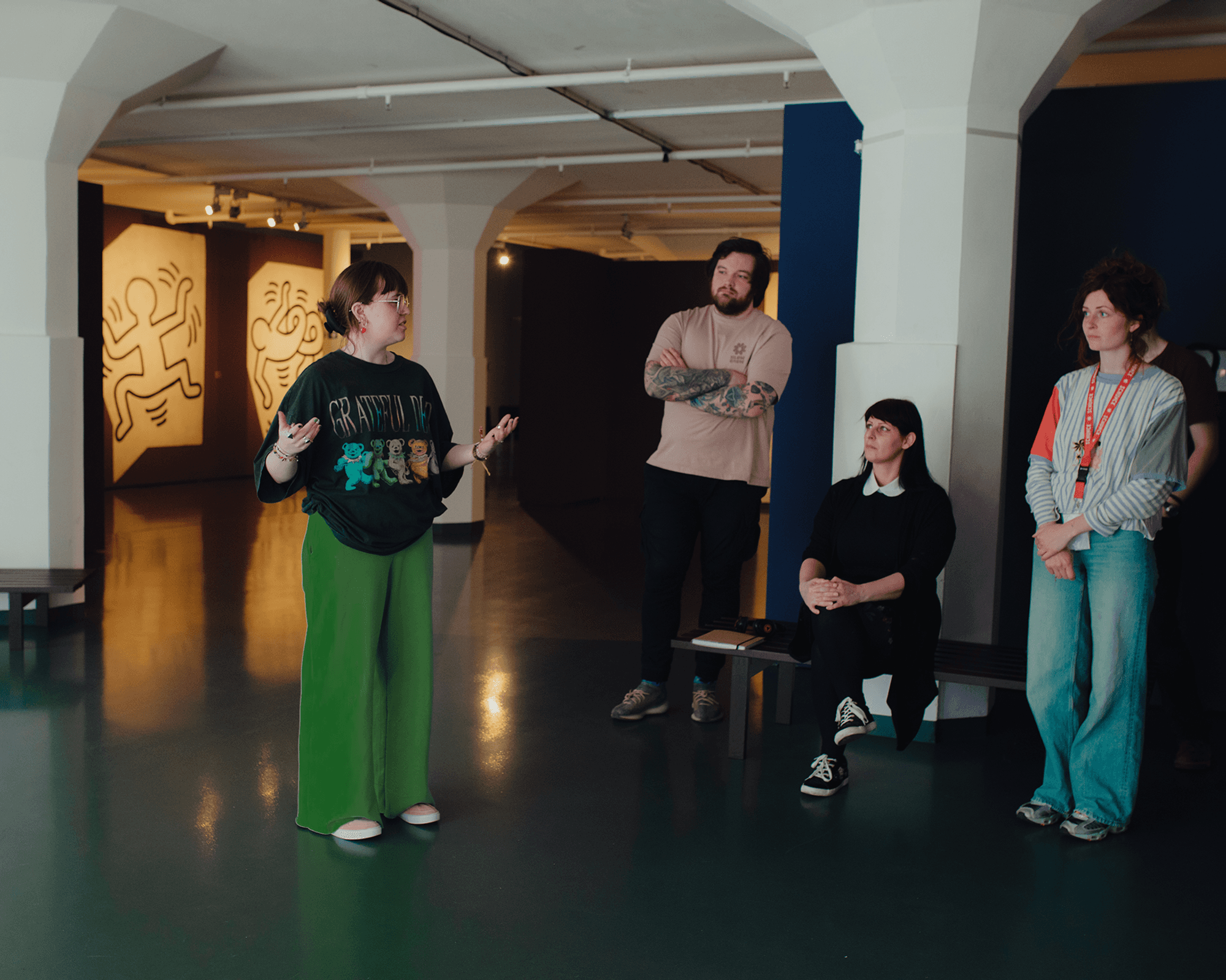 Jonge vrouw spreekt gepassioneerd voor een kleine groep tijdens een bijeenkomst in het museum, met op de achtergrond werken van Keith Haring.