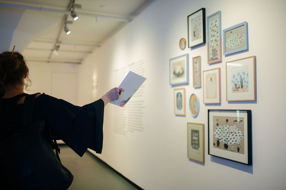 Verschillende ingelijste illustraties van Keetje Mans hangen aan de wand in het museum. Een vrouw kijkt en wijst naar de werken. 