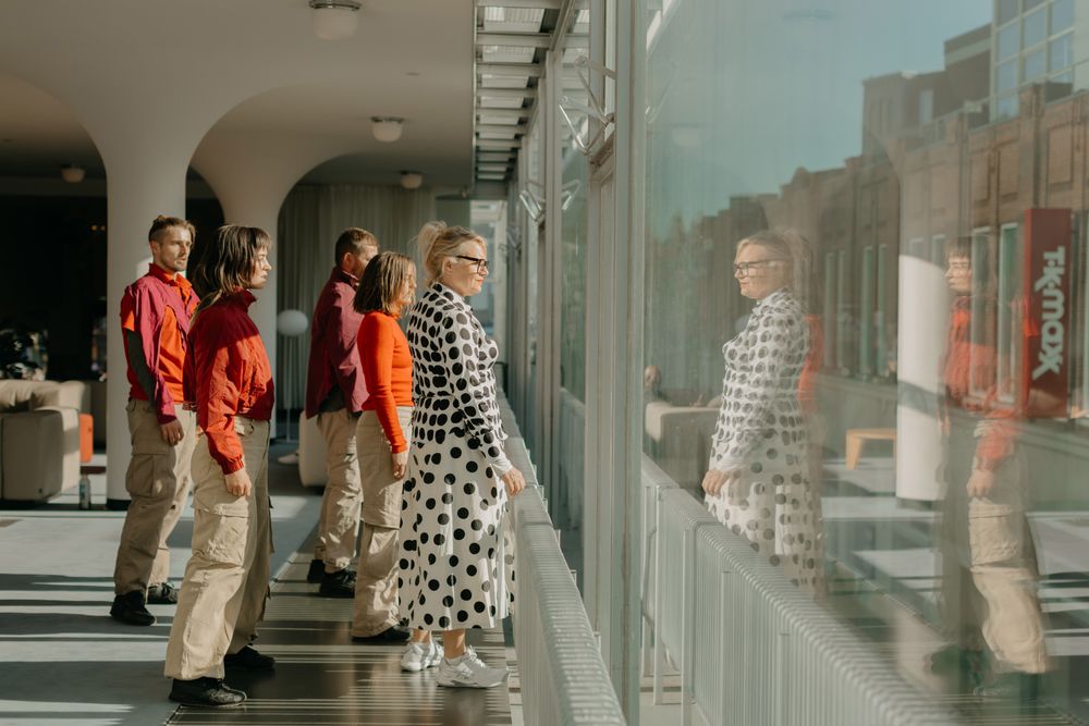 Groep mensen die in een lichte, moderne binnenruimte naast een groot raam staan en naar buiten kijken, met reflecties van de groep zichtbaar in het glas.