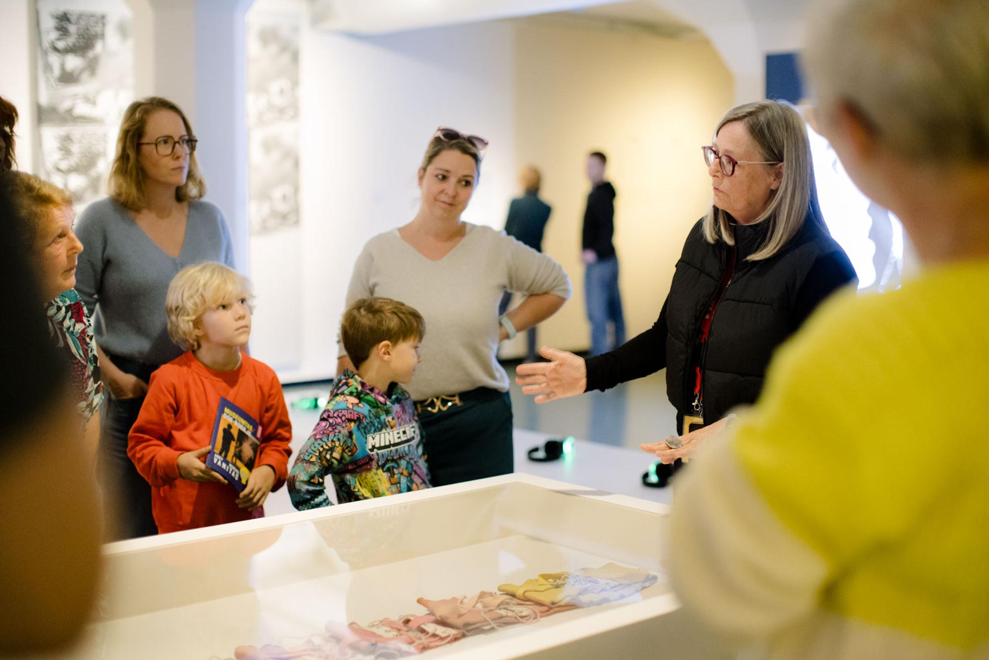 Bezoekers, volwassenen en twee kinderen staat bij vitrine tijdens rondleiding van Andy Warhol Vanitas. 