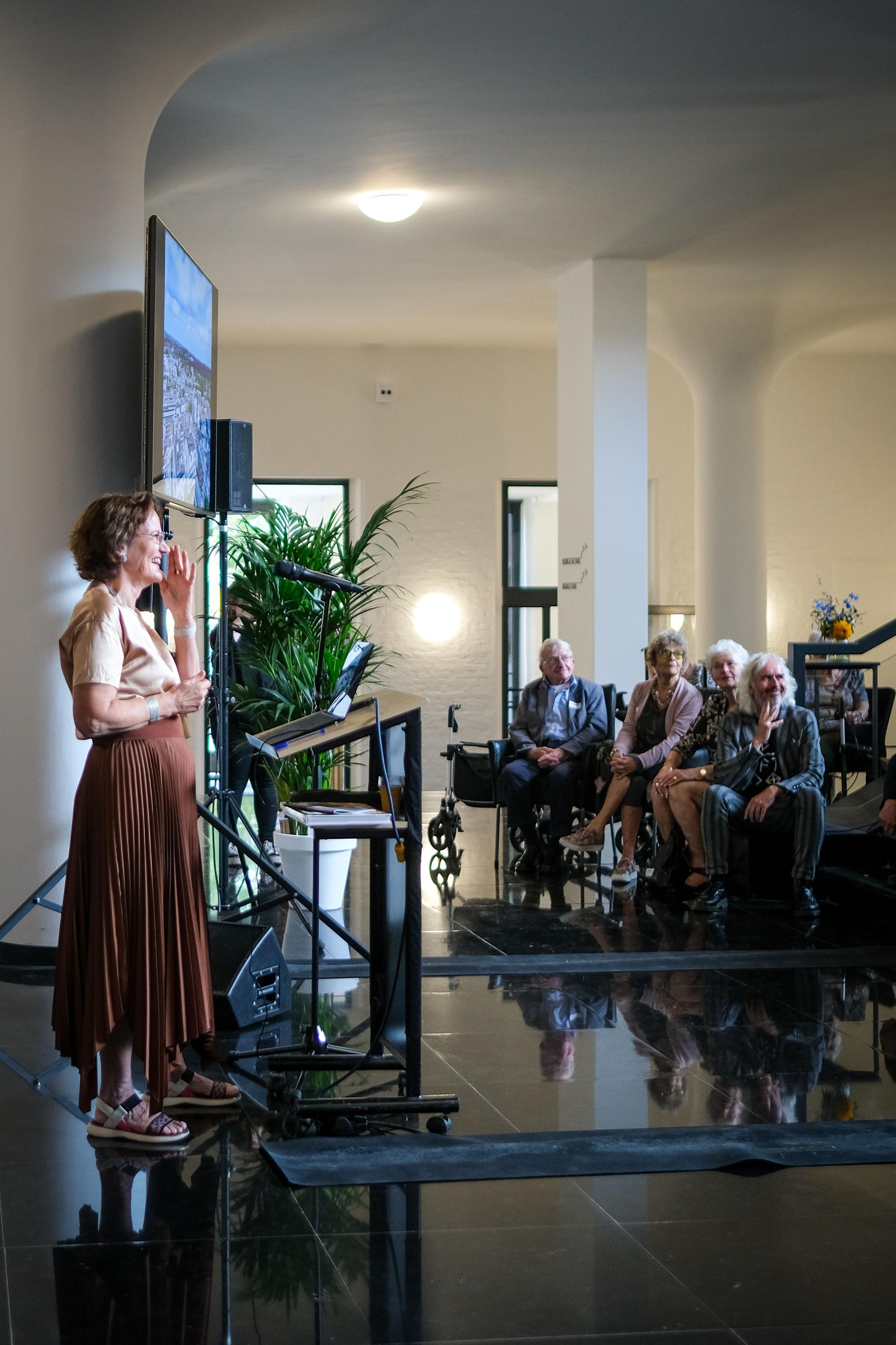 Francine Houben geeft een presentatie met een digibord aan bezoekers die op stoelen zitten in het Raadhuis.