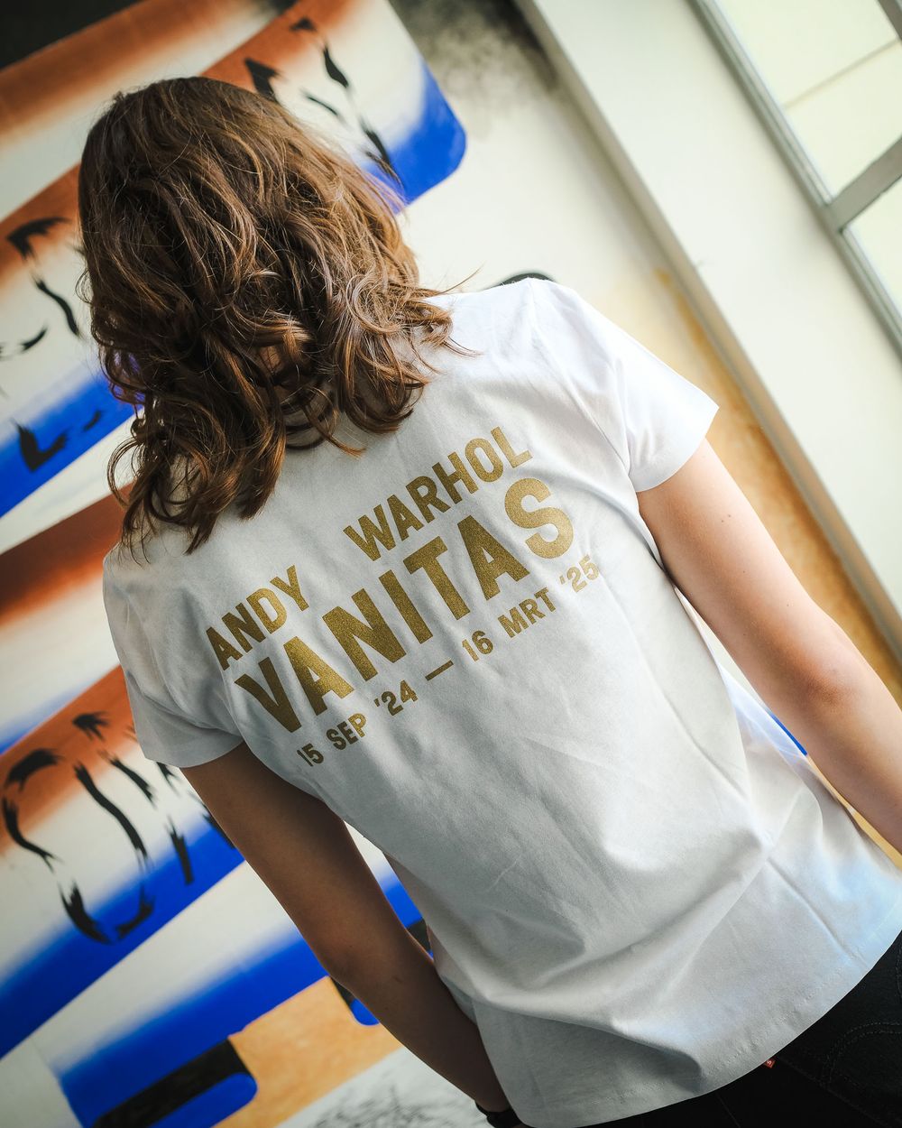 Vrouw draagt Andy Warhol merchandise shirt, gefotografeerd vanaf haar rug. 