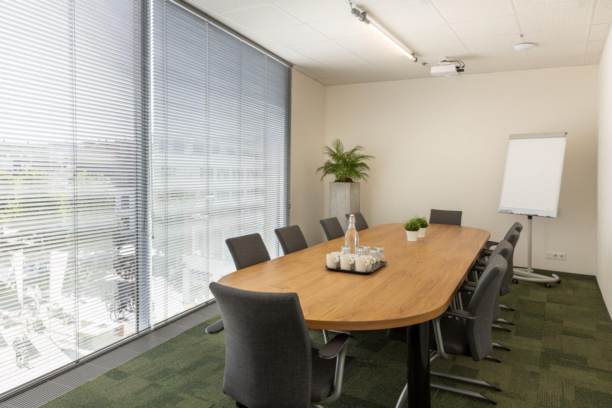 Vergaderruimte met lange houten tafel en stoelen. 