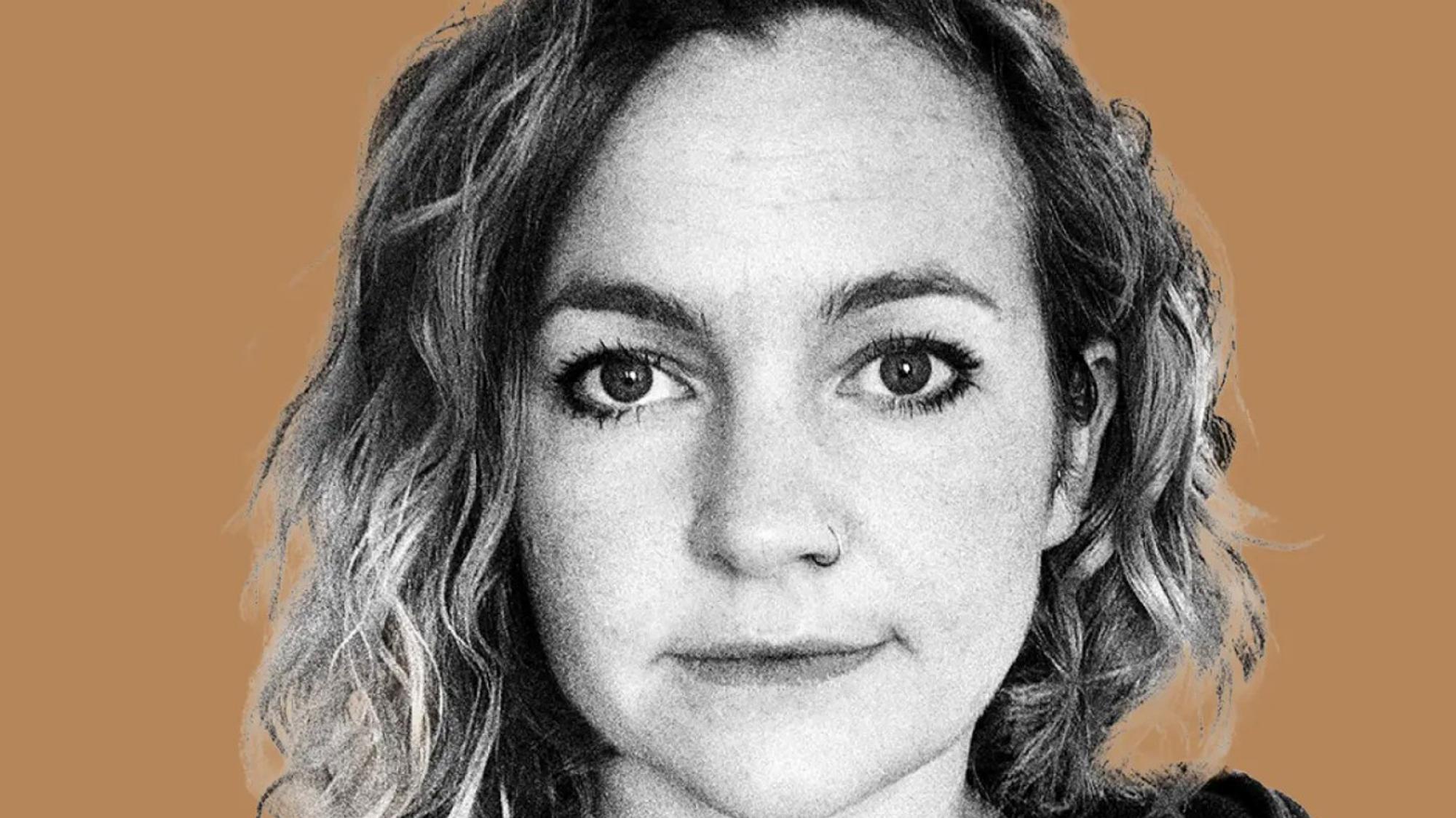 Zwart-wit portret van een vrouw met halflang, krullend haar en een neusring, voor een effen, bruin-oranje achtergrond. Ze kijkt recht in de camera met een neutrale gezichtsuitdrukking.
