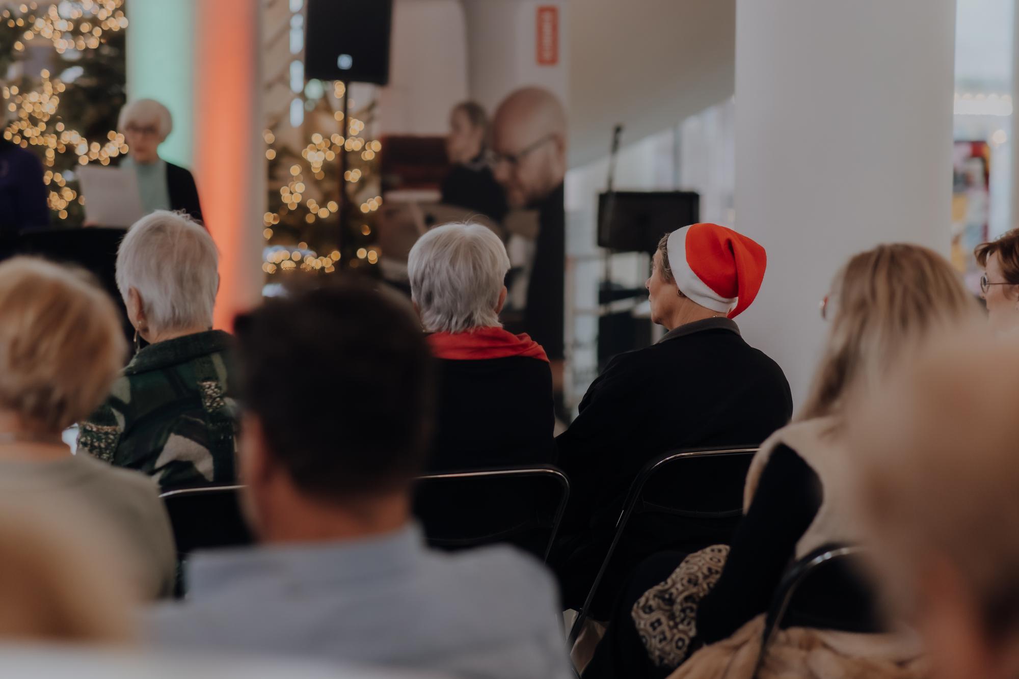 Publiek zit op stoelen in de hal van SCHUNCK en luisteren naar het winterconcert. een bezoeker draagt een kerstmuts.