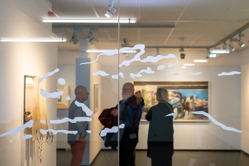 Op de voorgrond is glas te zien met daarop een kunstwerk. Op de achtergrond zijn een aantal mensen te zien die naar dit glas wijzen.