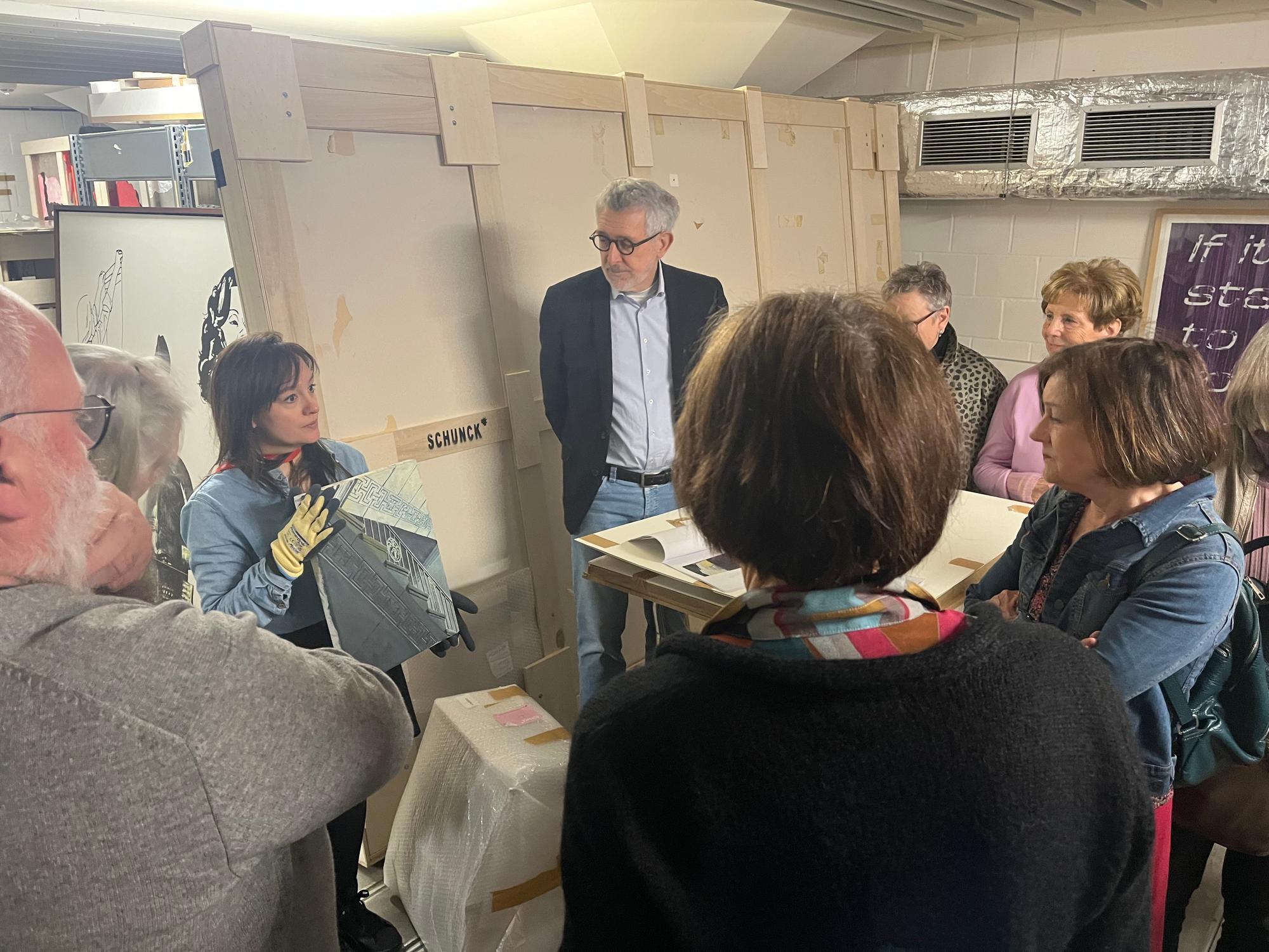 Een groep mensen staat in een cirkel en luistert naar een vrouw die uitleg geeft over een kunstwerk.