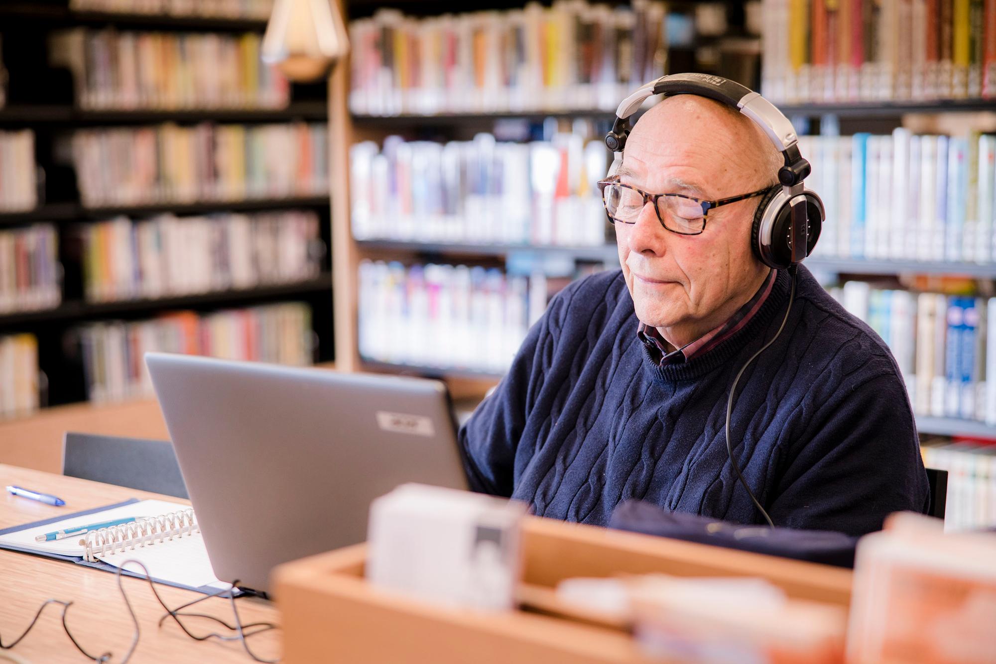 Man met koptelefoon achter de laptop volgt een taalcursus. 