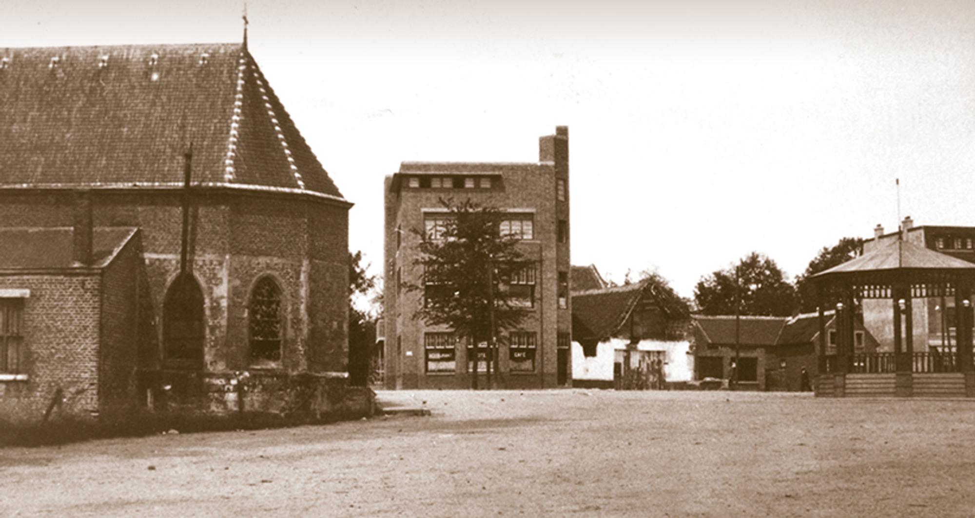 Historische foto van een dorpsplein met een kerkgebouw, een paviljoen en enkele oude panden.
