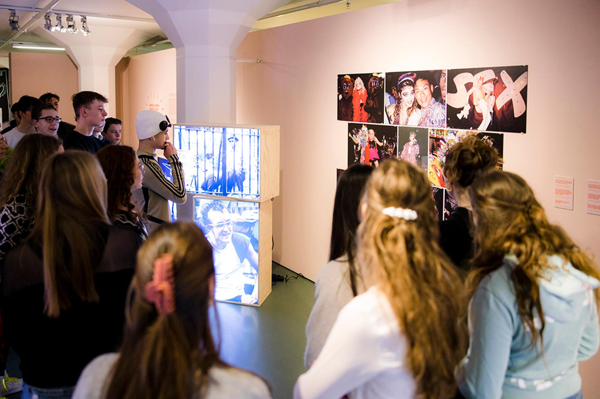Jongeren staan in het museum voor een paarse wand met foto's tijdens een rondleiding door de tentoonstelling 'Keith Haring, Grace House Mural' en bekijken aandachtig het werk aan de muur.