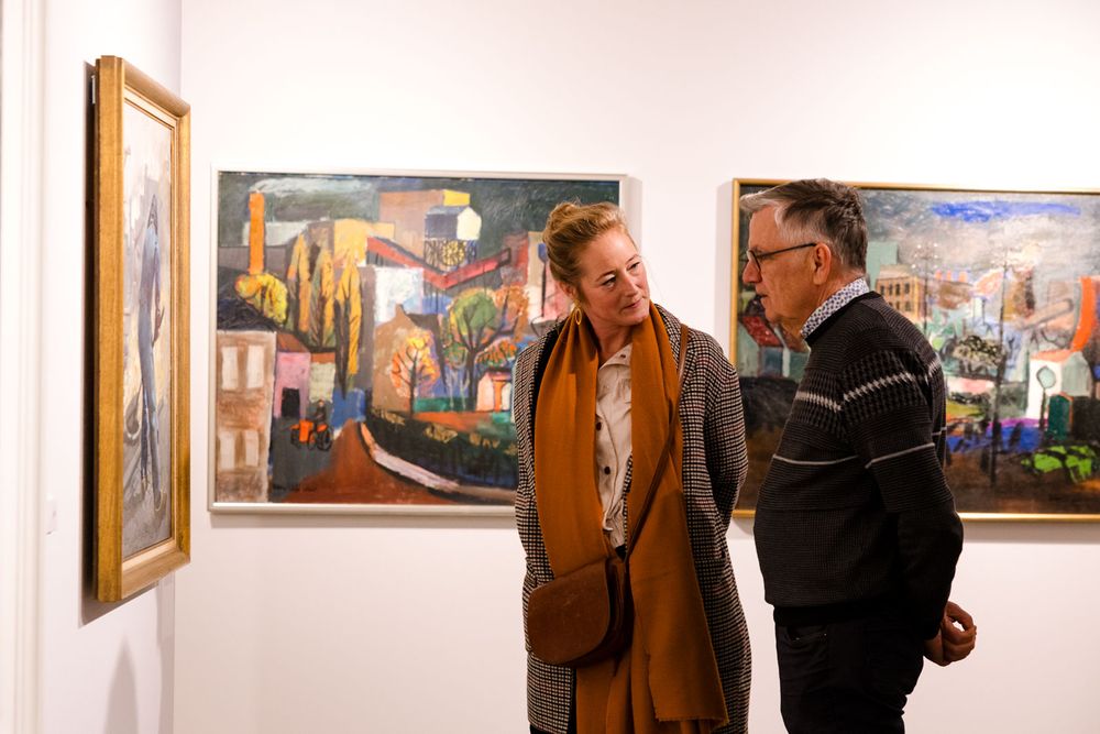 Twee bezoekers bekijken schilderijen van Limburgse kunstenaars tijdens de tentoonstelling Rooted in Change in het Nederlands Mijnmuseum.