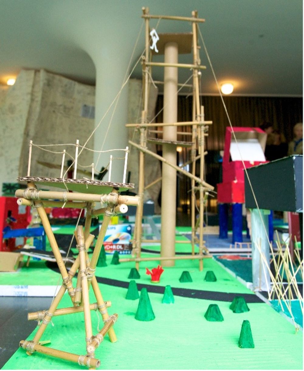 Maquette van een fantasierijk bouwwerk met torens, bruggen en constructies van bamboe en touw, opgesteld op een groene ondergrond.