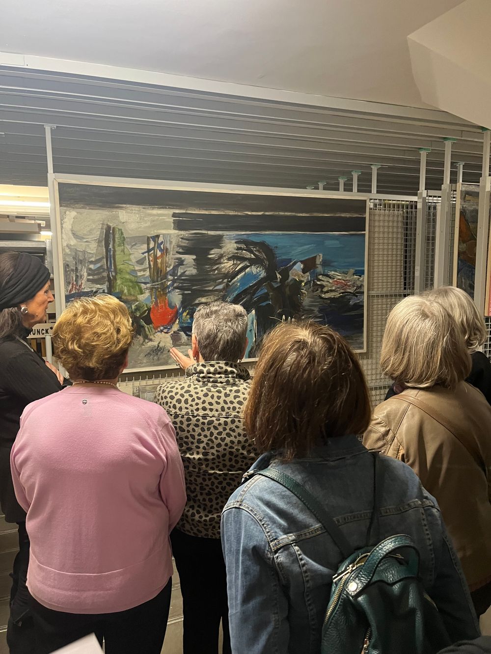Een groepje mensen kijkt aandachtig naar een kunstwerk dat in het depot staat, terwijl ze het zorgvuldig observeren.