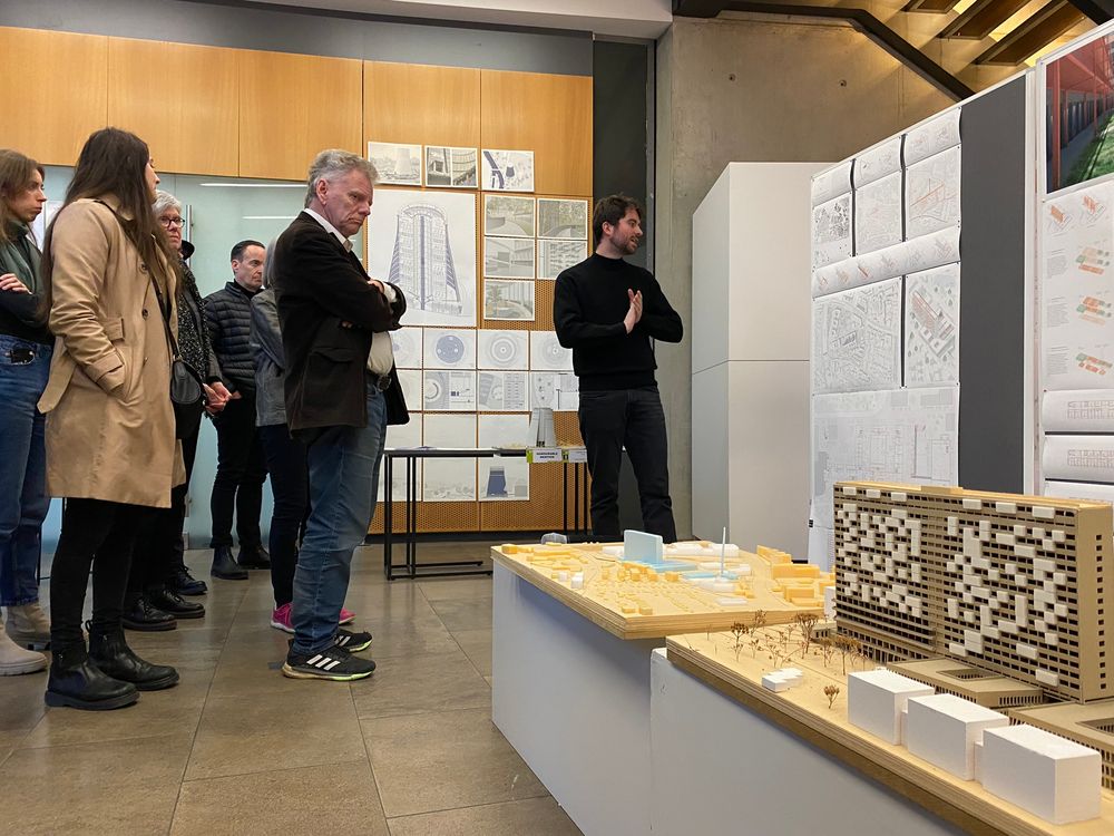 Bezoekers kijken naar maquettes en tekeningen van deelnemer EAP. Deelnemer staat naast zijn werk. 