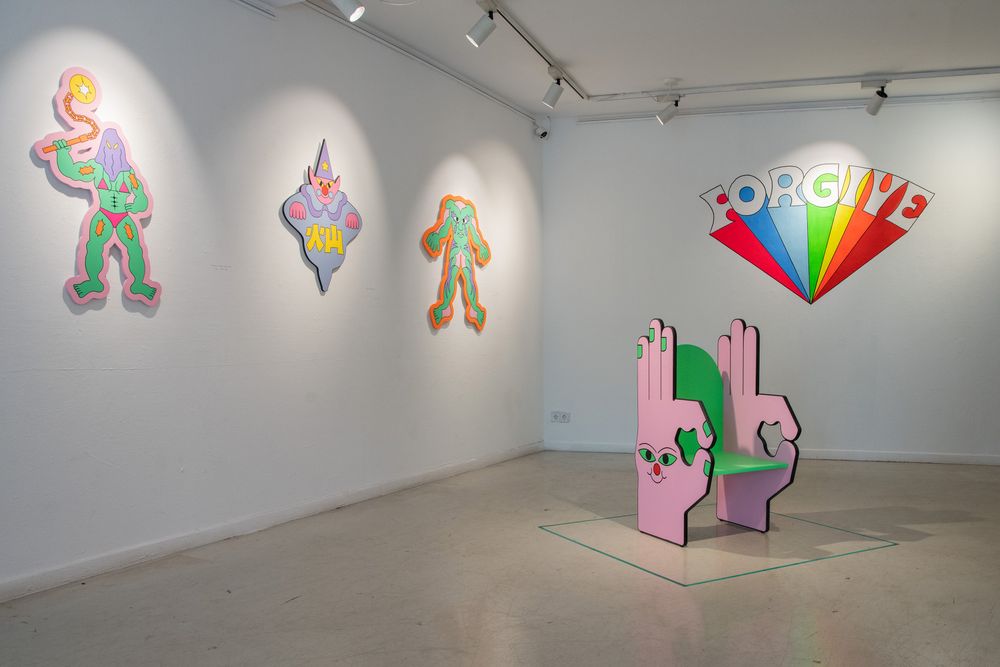 Tentoonstellingsruimte met kleurrijke sculpturen, wandwerken en een stoel van kunstenaar Irene Fresh, uitgevoerd in haar herkenbare speelse en grafische stijl.