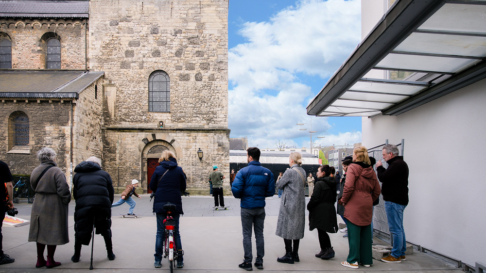 Bezoekers staan buiten te kijken naar skateboarders voor de Pancratiuskerk naast SCHUNCK.