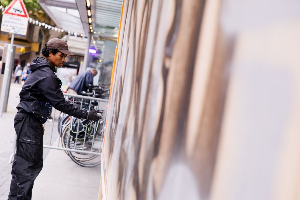 Kunstenaar Martinus Papilaja spuit met zwarte verf op een groot paneel in de stad