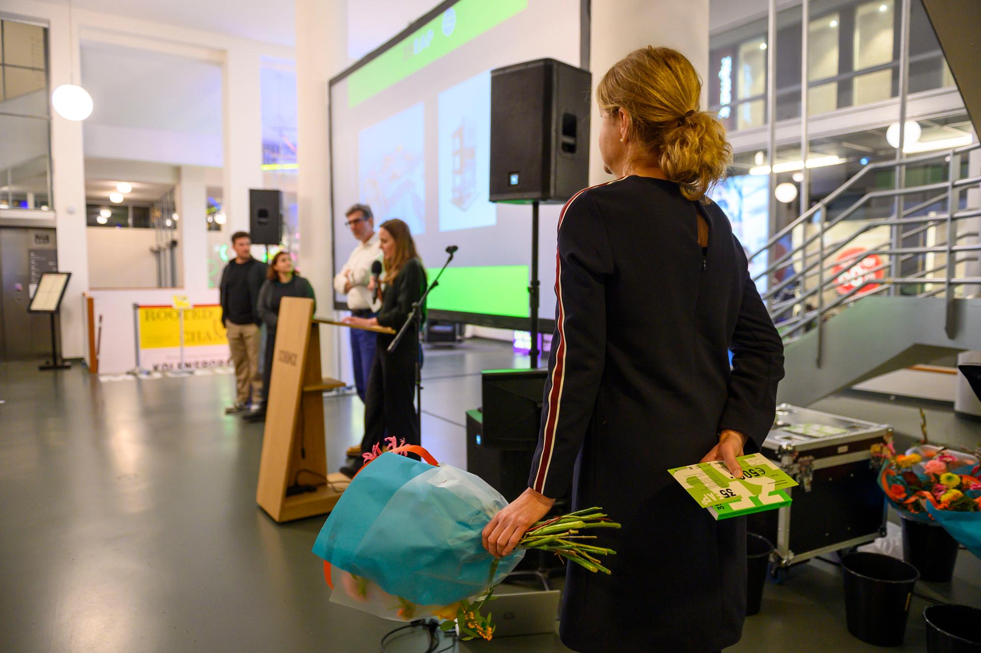 Een genomineerde wacht met bloemen en programmaboekje op de uitslag tijdens de prijsuitreiking van de Euregional Architecture Prize 2026 in SCHUNCK.