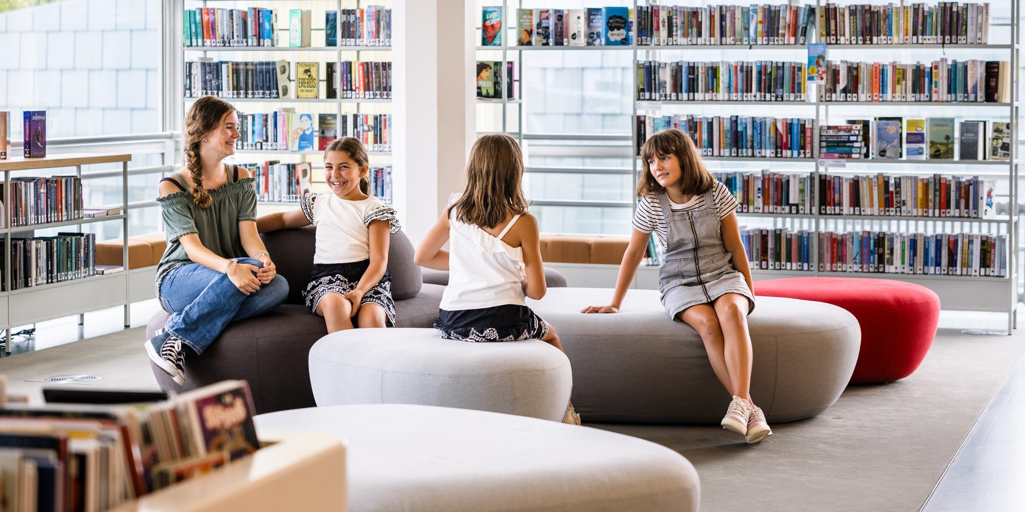Kinderen zitten samen in de bibliotheek tussen boekenkasten.