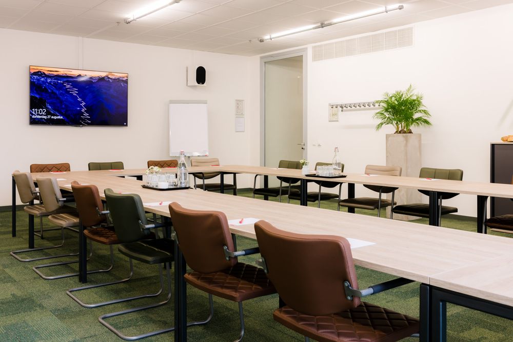 Vergaderzaal Zaal 2 in het SCHUNCK Glaspaleis, met tafels in een carré-opstelling, stoelen en een groot beeldscherm aan de muur.