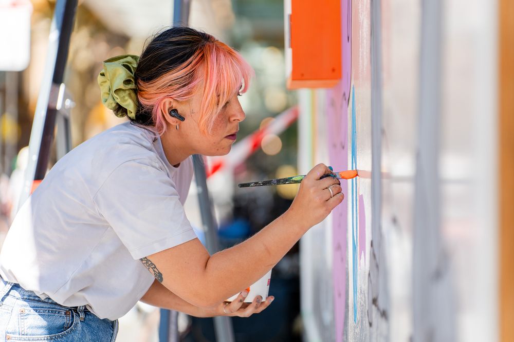 Kunstenaar Irene Fresh schildert met een penseel aan de nieuwe MODULE-wisselwand bij het Glaspaleis.