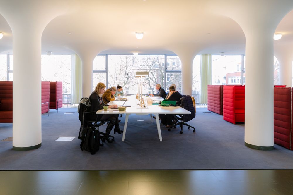 Mensen aan het werk met laptops op de werkplekken. Een grote witte tafel met bureaustoelen en lampen op tafel. 
