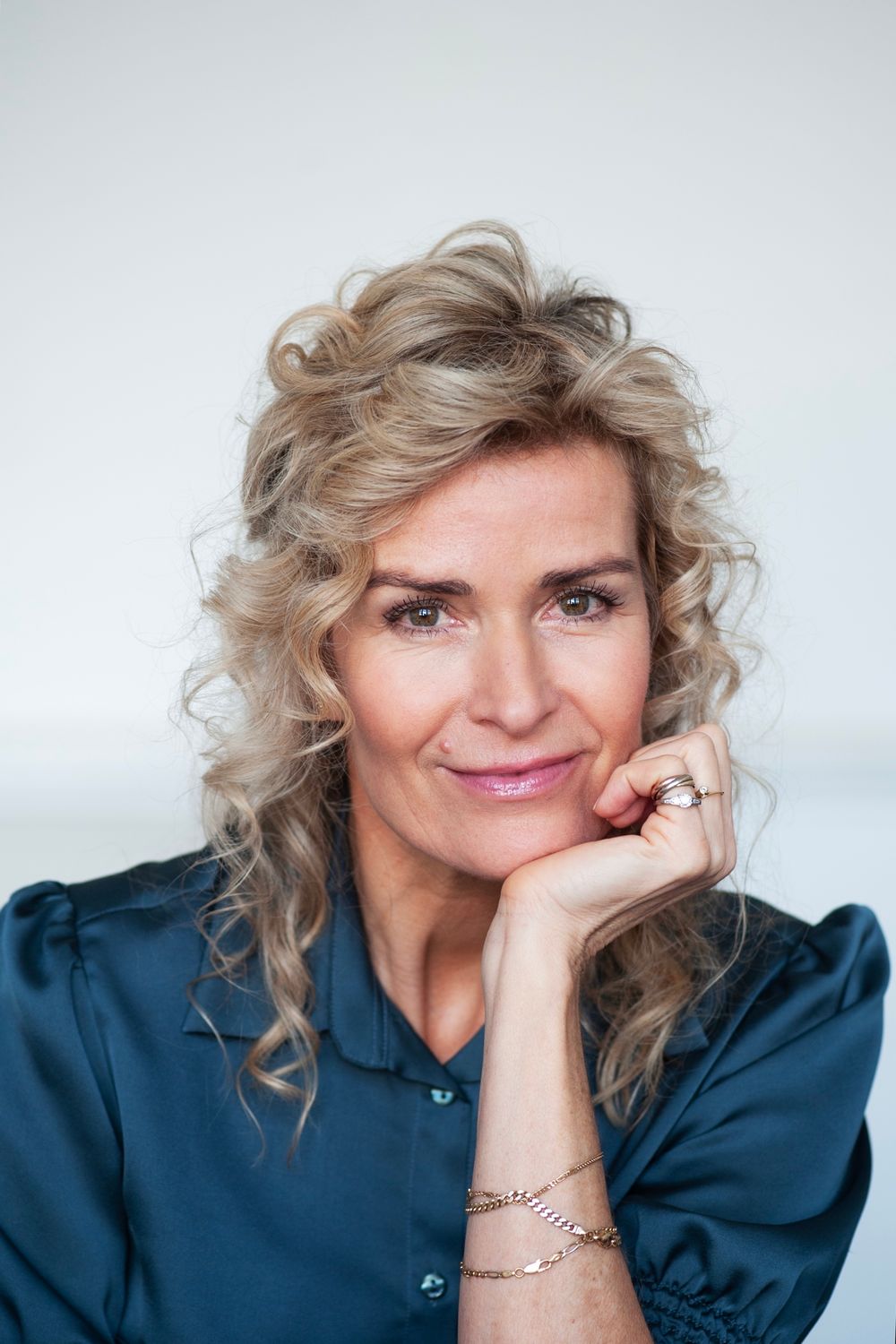 Portretfoto van schrijver Patricia Snel, zittend met het hoofd steunend op een hand. Patricia Snel draagt een donkerblauwe blouse en kijkt recht in de camera tegen een lichte, neutrale achtergrond.