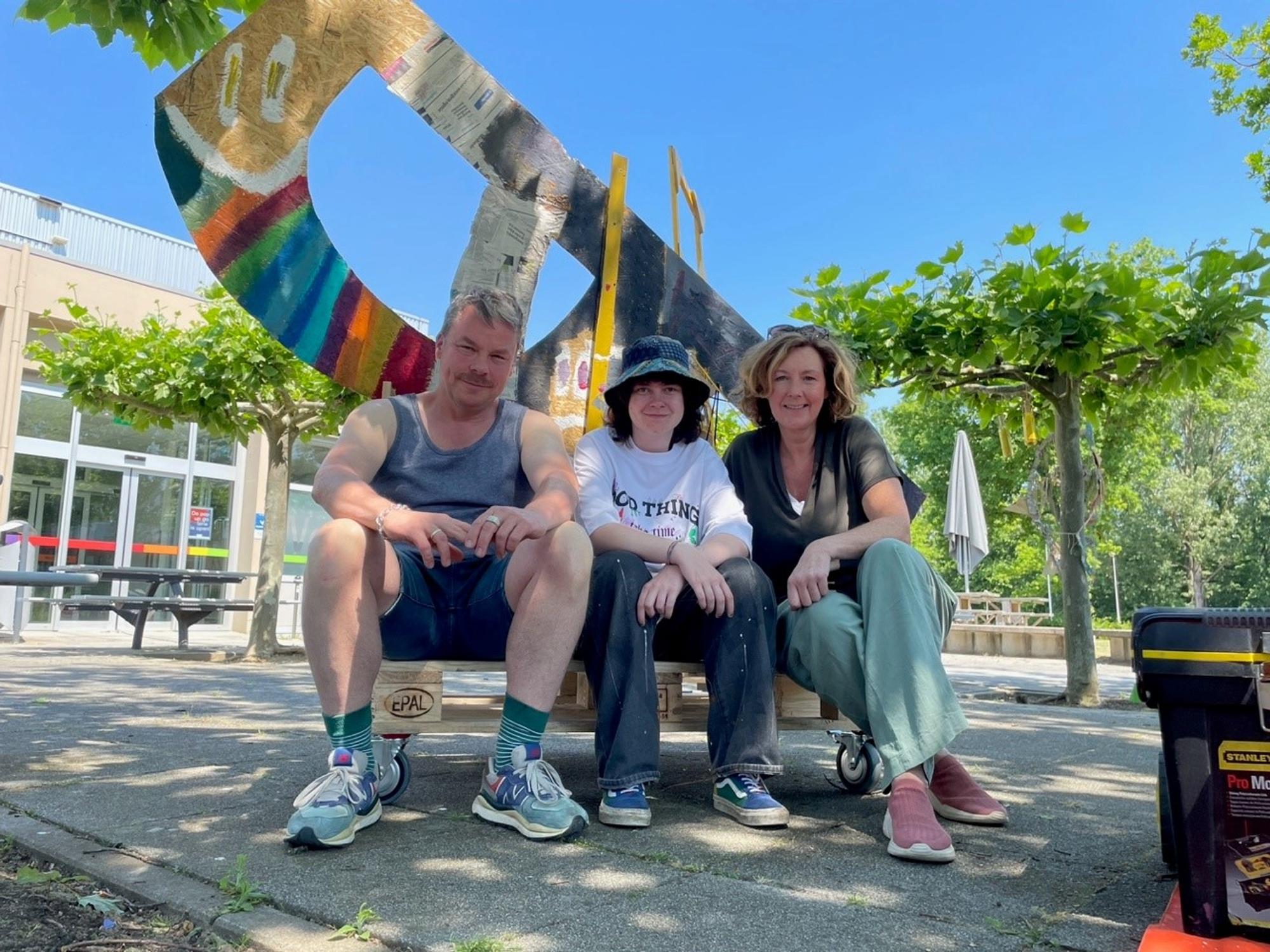 Huis Van Emoties Schunck David Bade 2023 David Bade zit met twee vrouwen op een pallet met wieltjes voor een kunstsculptuur buiten bij Mondriaan.