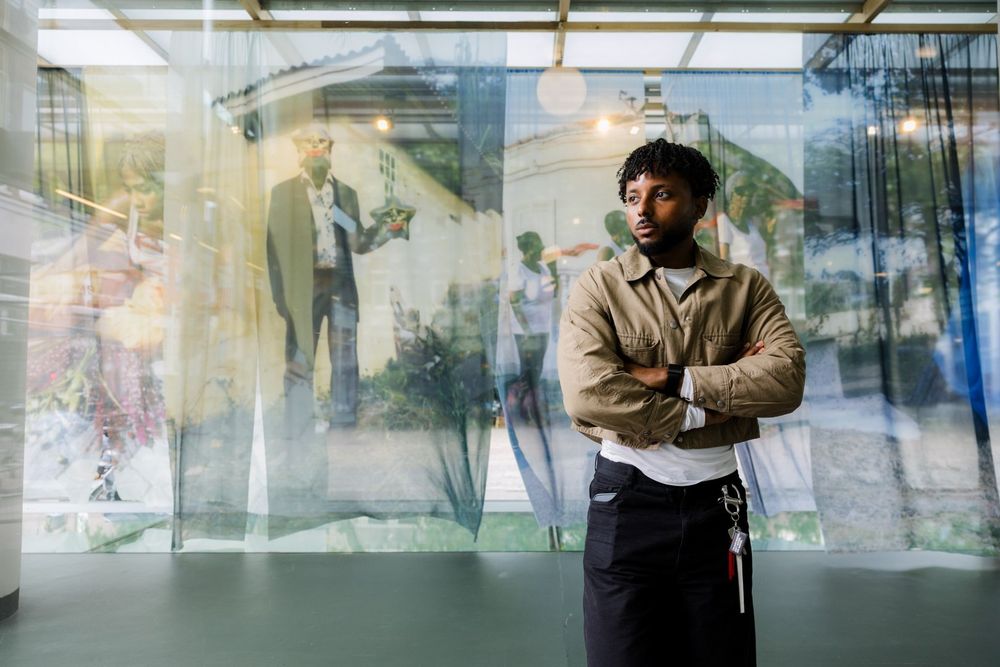 Kunstenaar Kevin Osepa voor zijn werk in de vitrine, waarin foto's op textiel persoonlijke herinneringen oproepen.