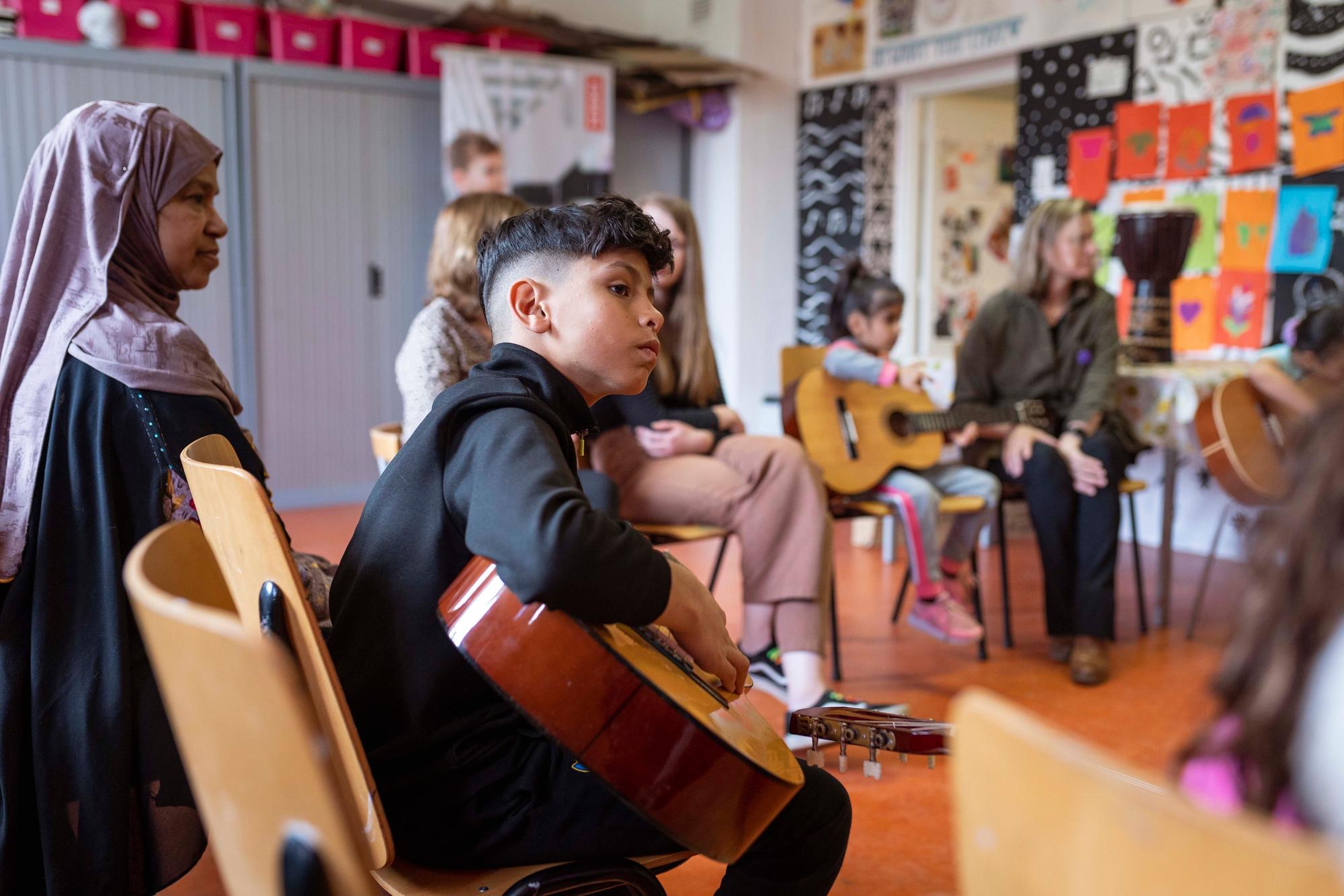 Jongeren en ouders zitten in een kring met gitaren en krijgen muziekles.