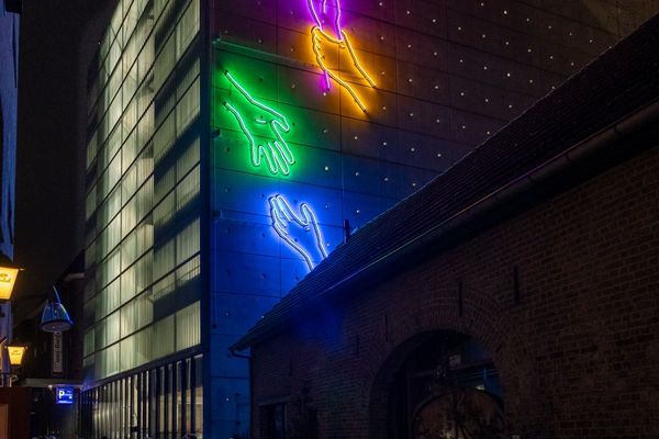 Neonkunstwerk van kleurrijke handen van Chaim van Luit op de gevel in de Plaarstraat, gezien vanaf de straat.