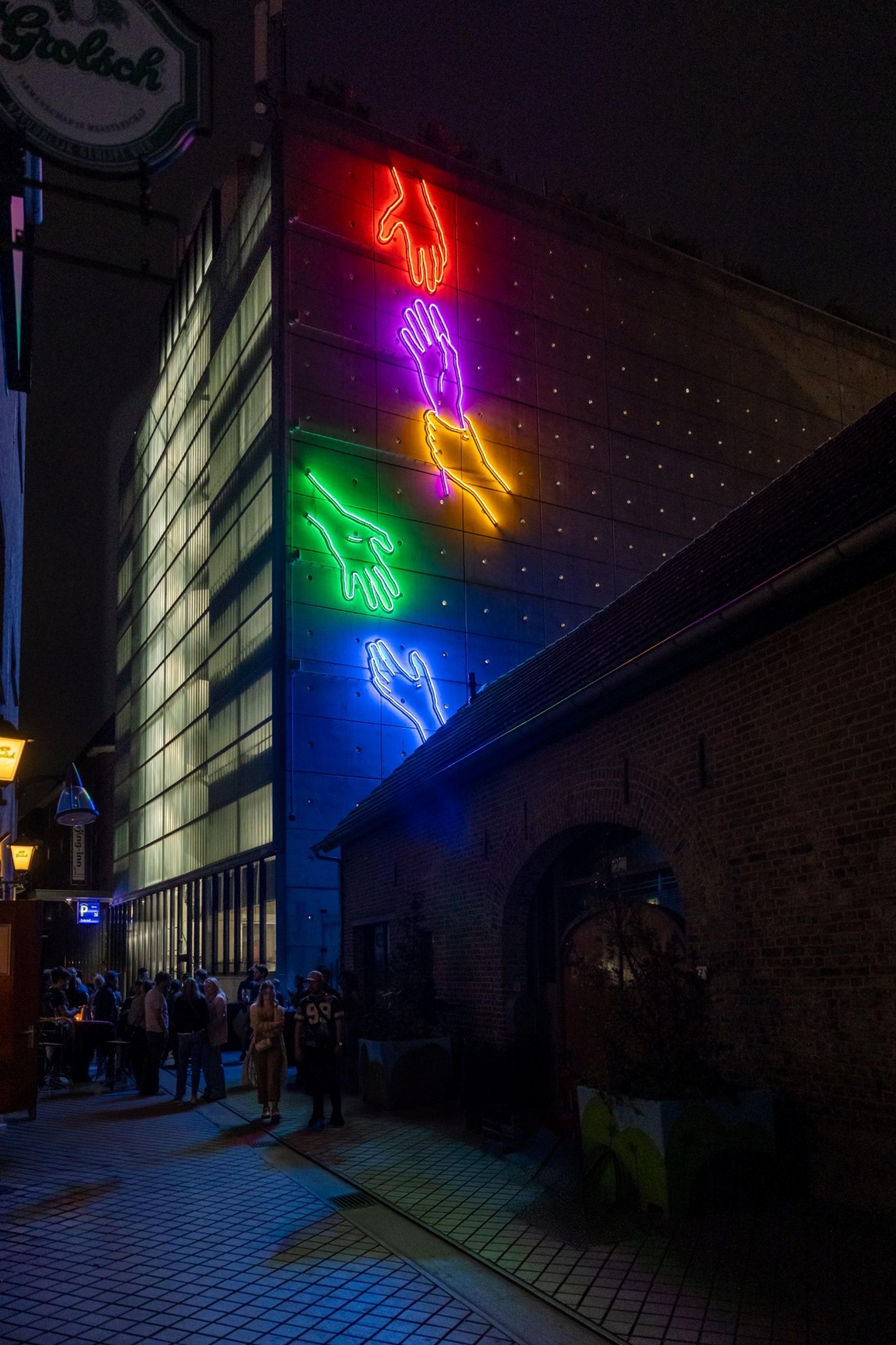 Neonkunstwerk van kleurrijke handen van Chaim van Luit op de gevel in de Plaarstraat, gezien vanaf de straat.