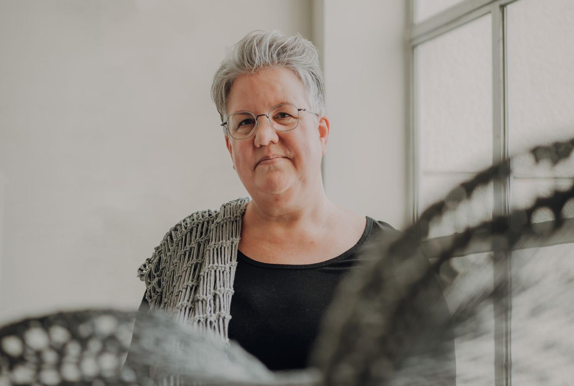 Portret van Jacqueline Muitjen met een gehaakt werk over haar schouder. 