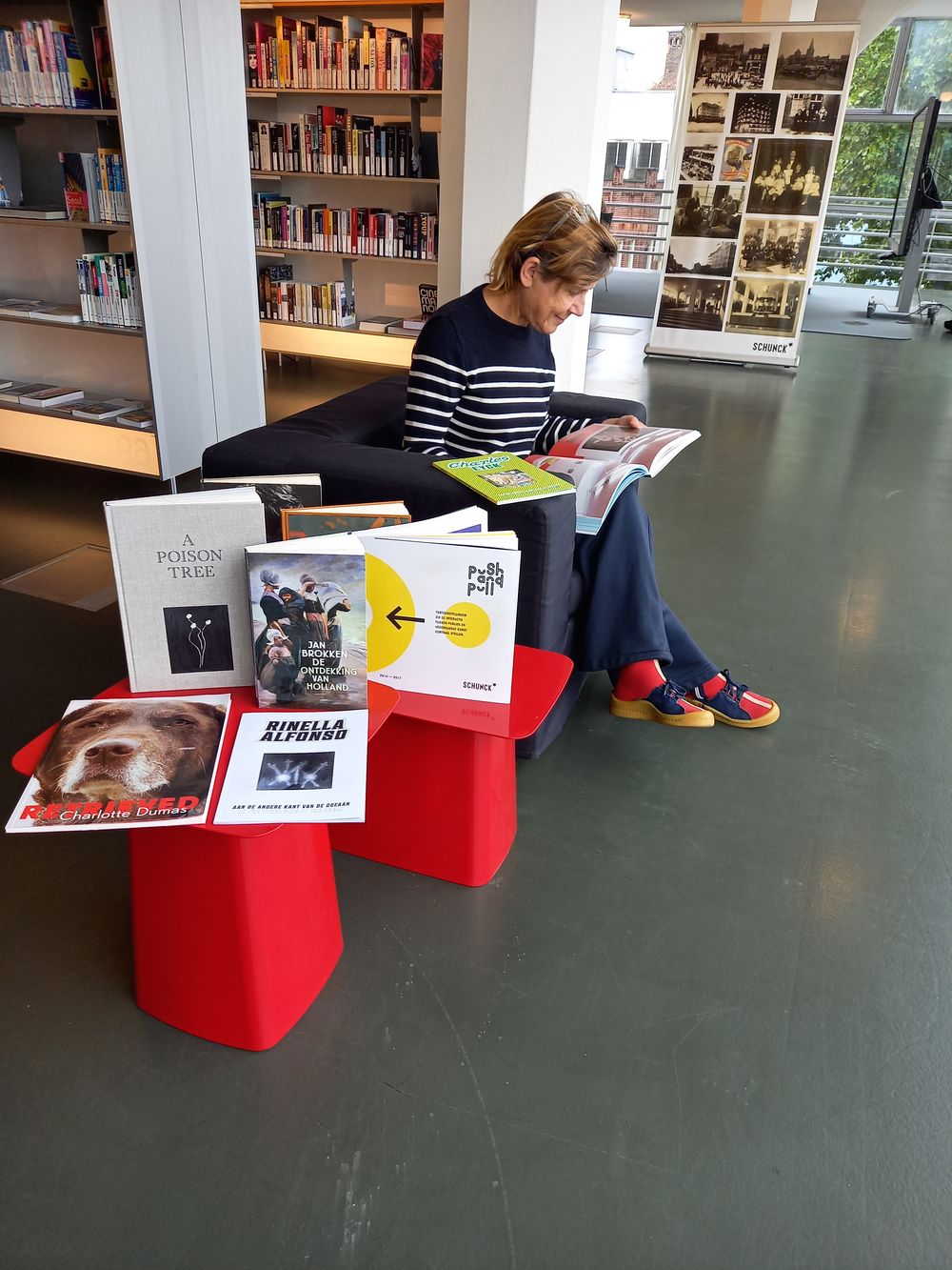 Janna Navis zit lezend in een fauteuil in de bibliotheek van SCHUNCK. Op een rood tafeltje voor haar liggen verschillende boeken uitgestald, waaronder Retrieved van Charlotte Dumas. 