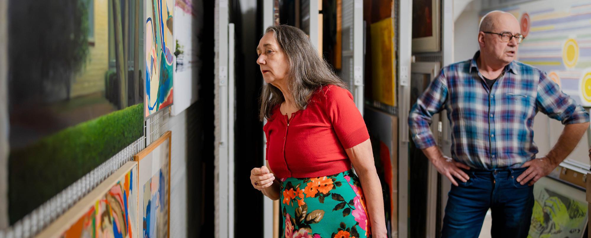 Deelnemer van de Groene Golf bekijkt schilderijen van dichtbij in een depotruimte met schuifrekken.