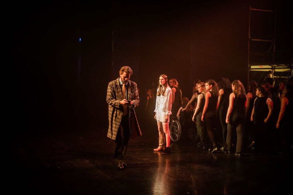 Scène uit de Eve Rockopera van SCHUNCK Muziek en Dans. Een man en vrouw op de voorgrond, met een groep acteurs in zwart gekleed op de achtergrond.