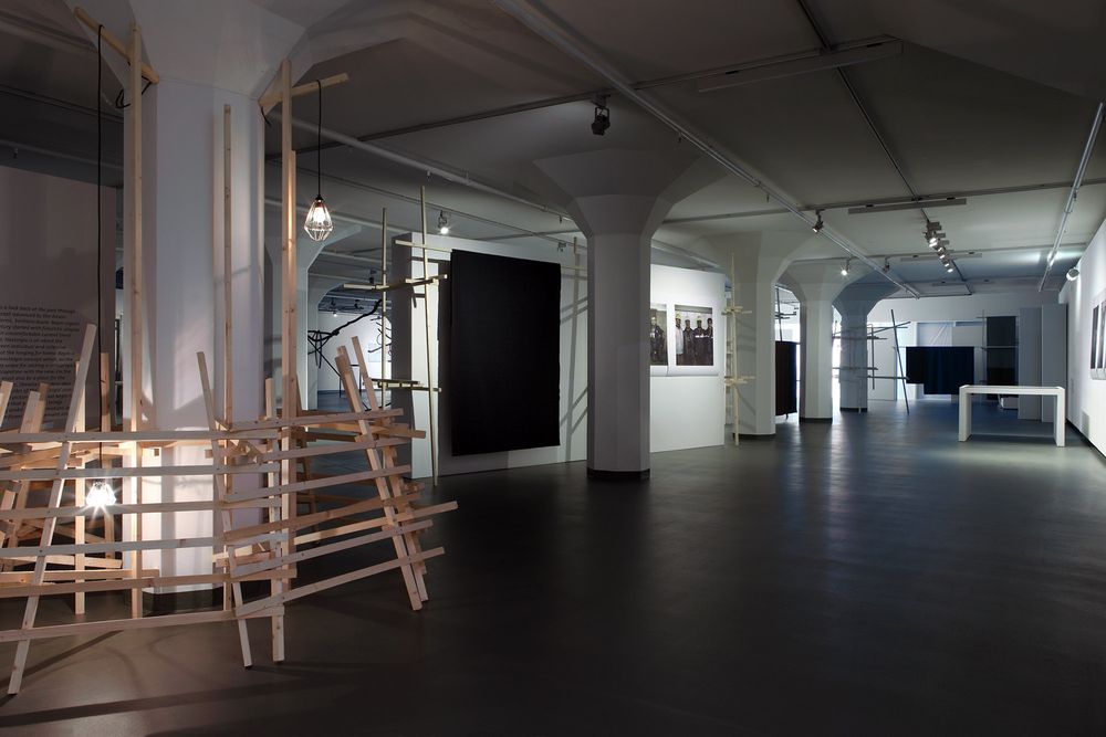 Museumzaal tijdens expositie 'Oet Der Stub', houten palen aan elkaar geconstructureerd en foto's aan de wand.