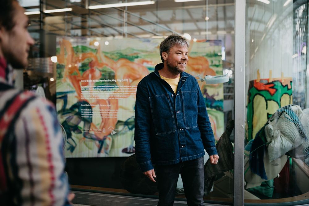 Portret van David Bade in een spijkerjas voor zijn werk in de vitrine van SCHUNCK.