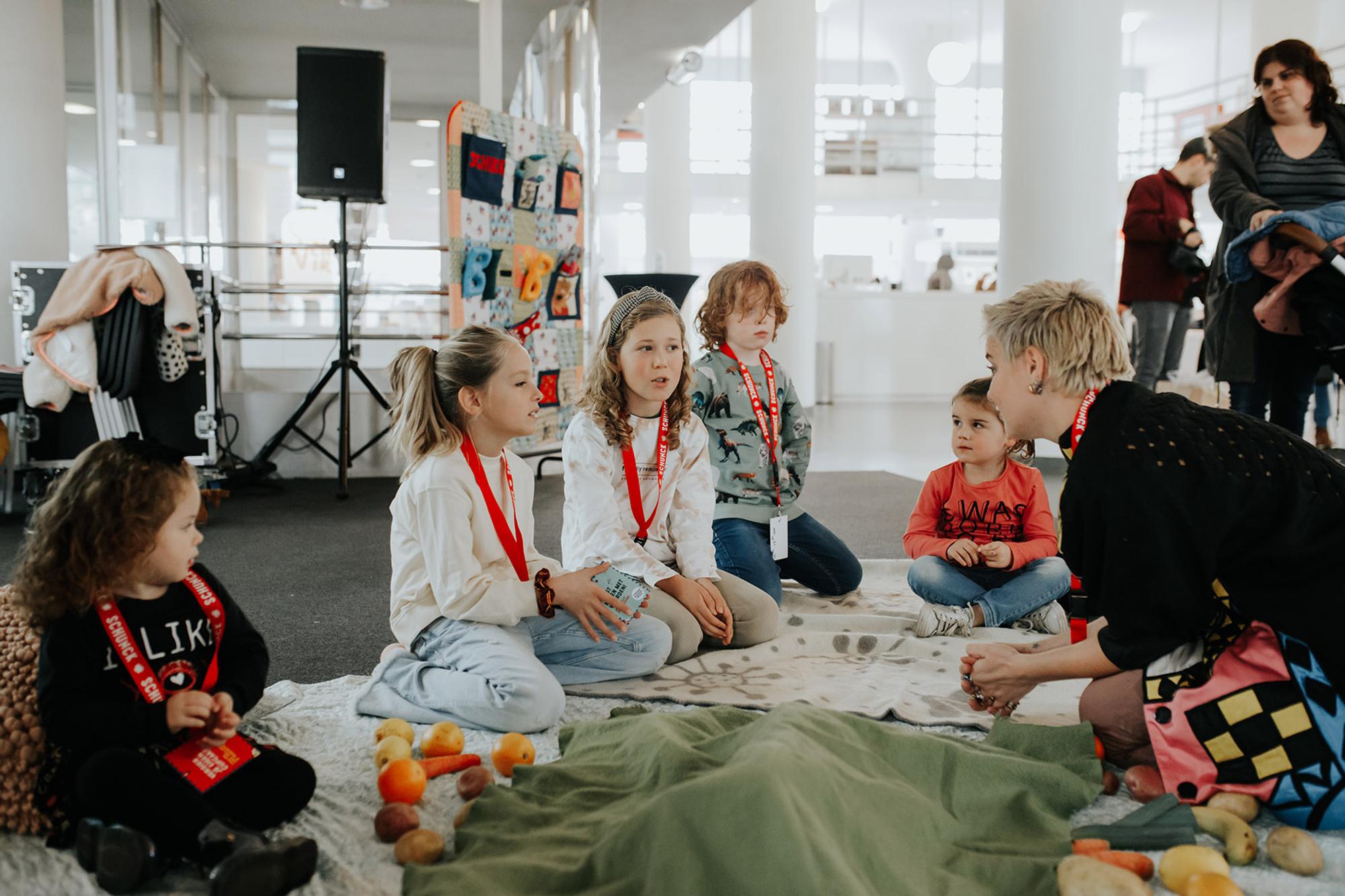 Workshop leidster met kinderen zitten op de kleden en praten met elkaar. Voor hen liggen groenten. 