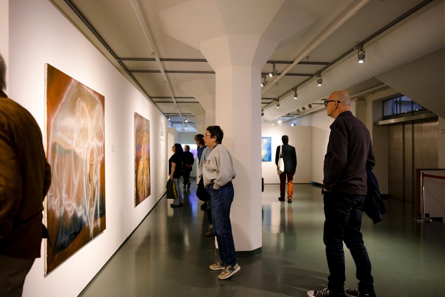 Bezoekers bekijken schilderijen in een moderne museumzaal met witte muren, glanzende vloer en gerichte verlichting.

