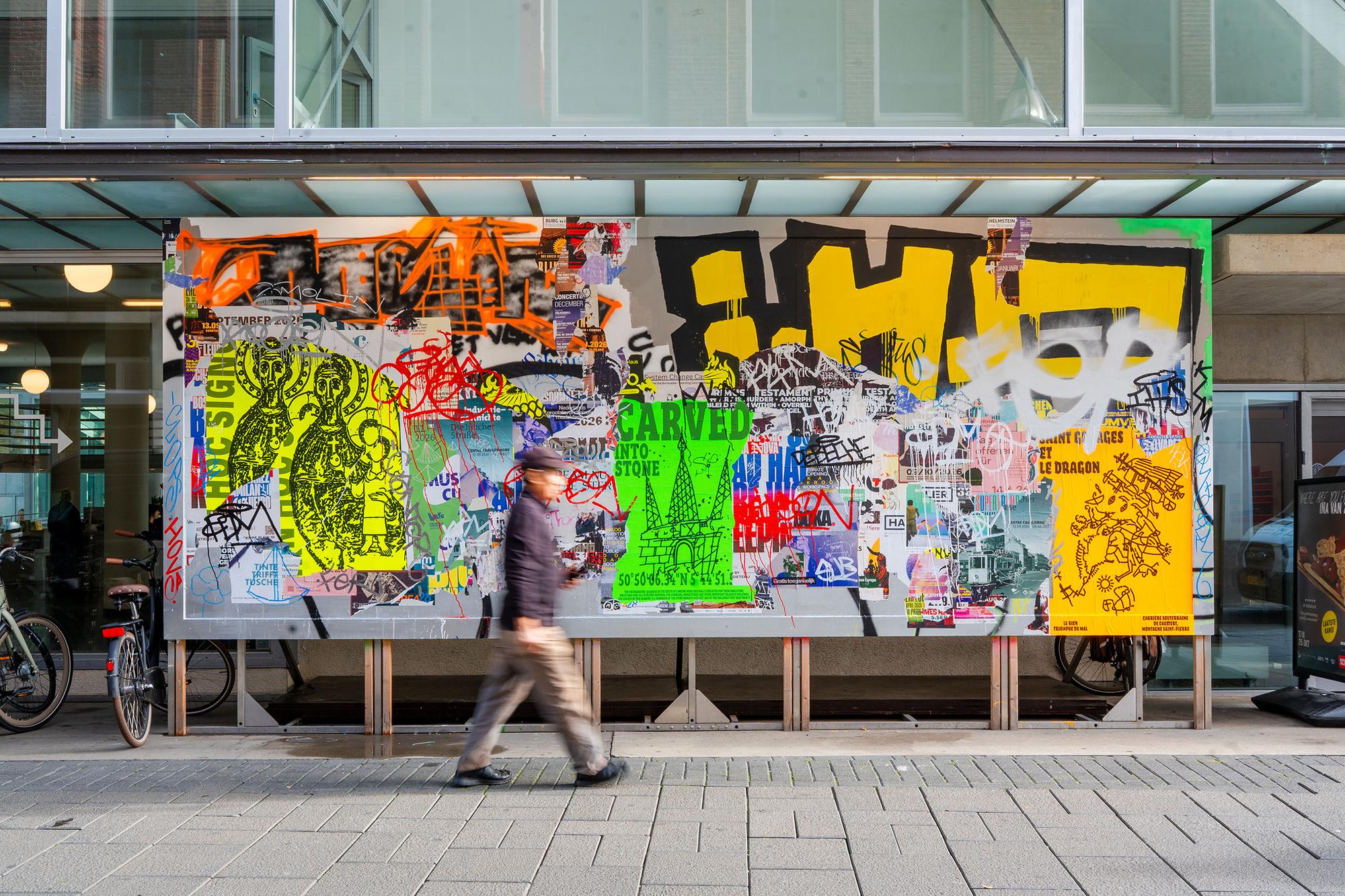 Kleurrijk kunstwerk met posters, graffiti en typografie in geel, groen, oranje en zwart aan de gevel van het Glaspaleis in Heerlen. Op de voorgrond loopt een voorbijganger.