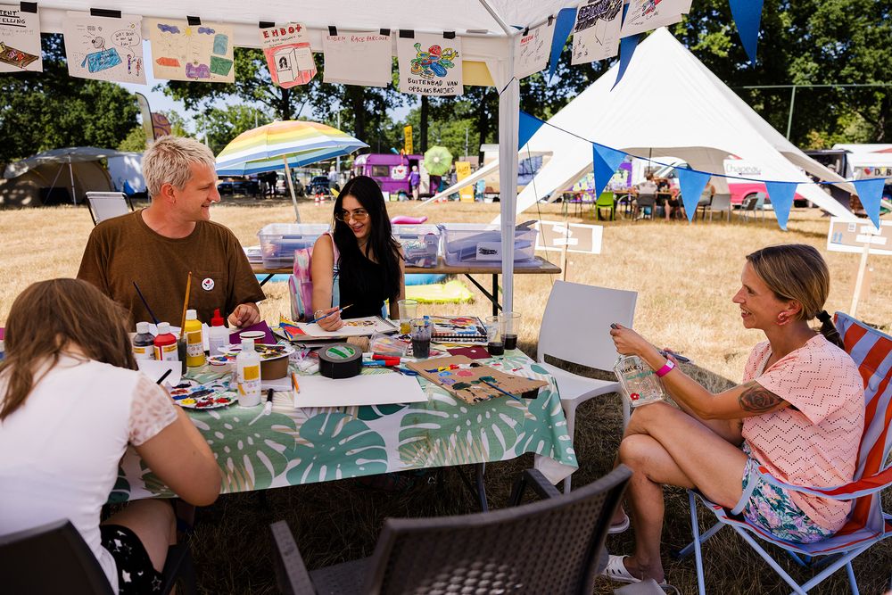Maarten Bel en bewoners zitten rond een tafel vol tekeningen, verf en knutselmateriaal en werken samen ideeën uit.
