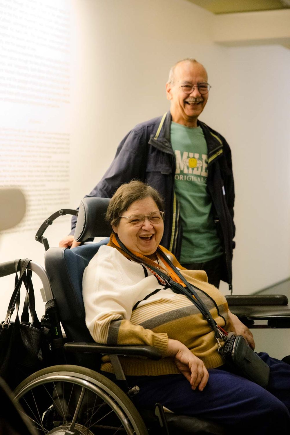 Vrouw in een rolstoel en man lachend in het museum. 
