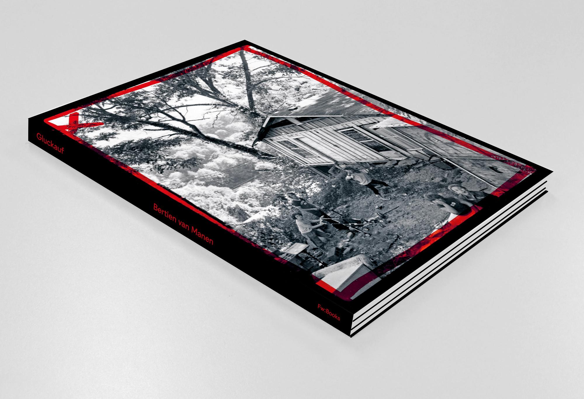 Fotoboek 'Gluckauf' van Bertien van Manen, liggend op een witte ondergrond, met een zwart-wit foto van spelende kinderen voor een houten huis op de cover en rode accenten in het ontwerp.