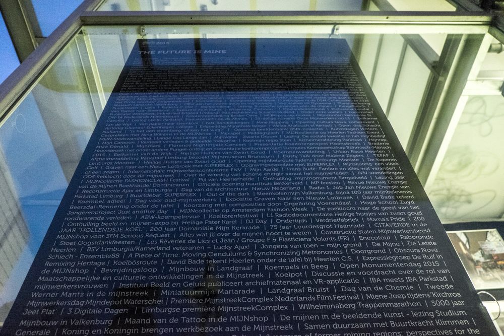 Detailfoto van een zwarte plaquette onder glas bij SCHUNCK, met in witte letters een lange lijst aan evenementen en namen, onderdeel van de installatie ‘The Future is Mine’.