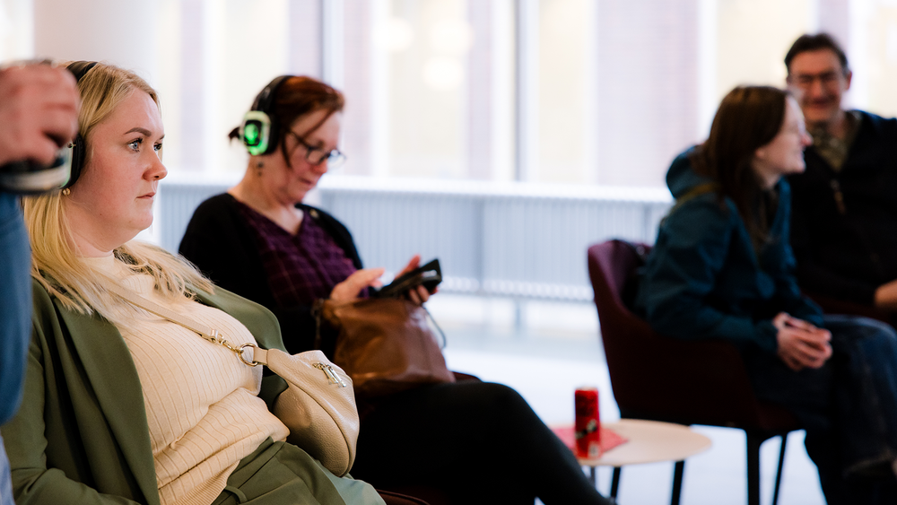 Bezoekers zitten op stoelen met silent disco koptelefoons op. 