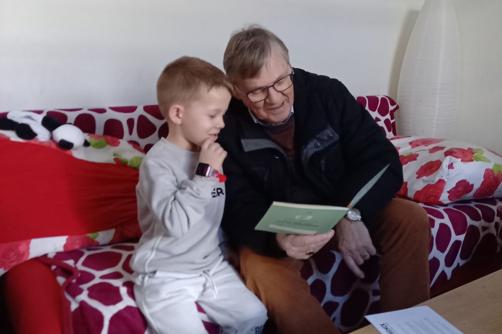 Vrijwilliger Voorleesexpress, man zit met een kind op een bank en lezen samen een boek.