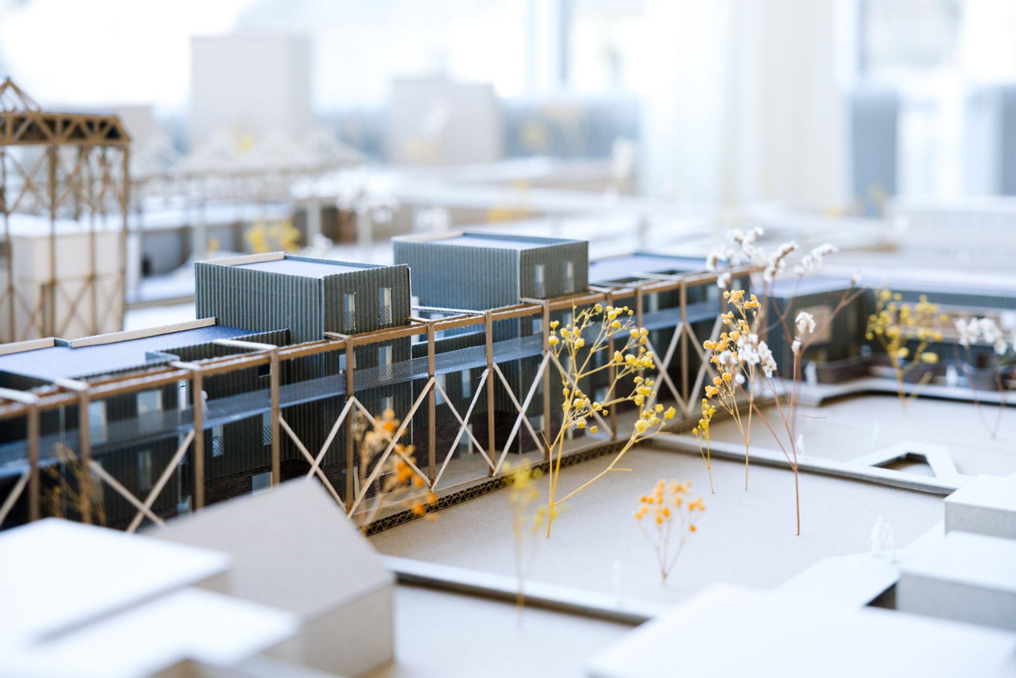 Maquette van een modern architectonisch gebouw met verhoogde structuren, metalen gevels en schaalbomen.